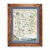 Hand-drawn map of Rocky Mountain National Park in a pine frame with blue mat, showcasing earth tones of green and beige. Illustrations feature landmarks such as Trail Ridge Road, Mount Ganby, Estes Park, and Alpine Visitor Center, alongside flora and fauna like bobcat, snowshoe hare, Indian paintbrush, and wild rose. Dimensions: 18x24 inches.