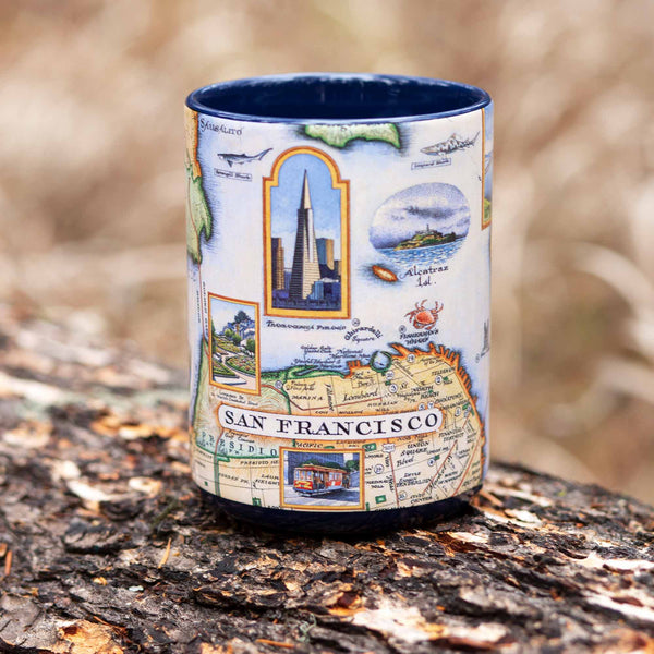 Blue 16 oz San Francisco Bay Map Ceramic Mug with handle sitting on a log in the forest. 