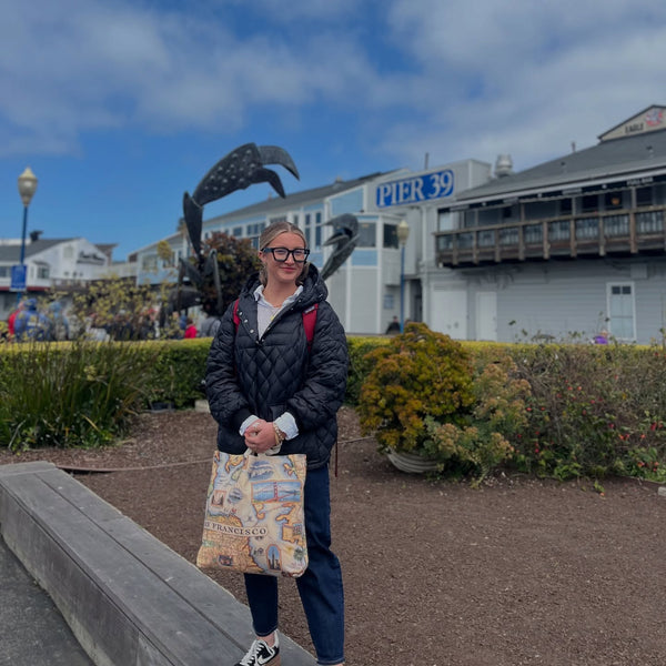 Person standing outdoors with a scenic background featuring a building and statues.
