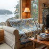 Cozy living room with a map blanket draped over a chair, stone fireplace, and view of water and trees.