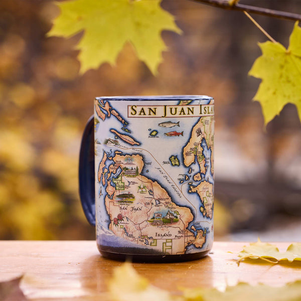 Mug with a map design of San Juan Island on a wooden surface with autumn leaves.