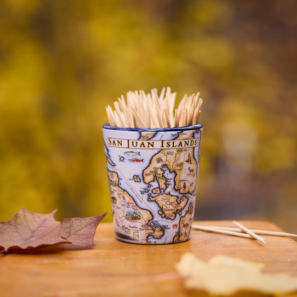 Shot glass with map design containing toothpicks on a wooden surface with blurred natural background