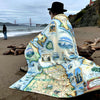 Elder women sitting on the beach wrapped in a aSan Francisco fleece blanket. In the background is the Golden Gate Bridge