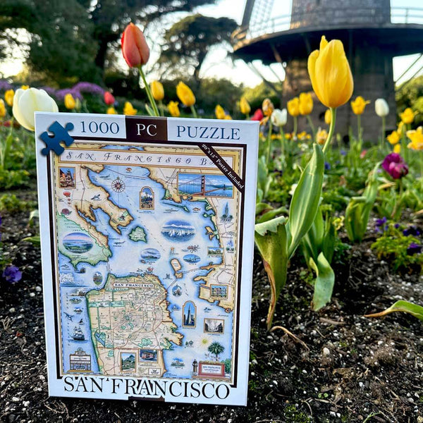 San Francisco puzzle box sitting a garden  next to tulip and the bottom of a windmill. 