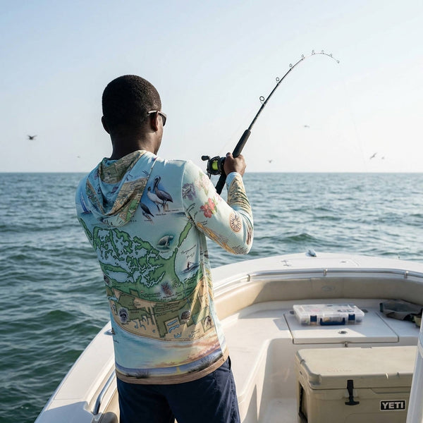 Man fishing on a boat with a colorful shirt and sunglasses, wearing a Sanibel & Captiva Islands sun shirt