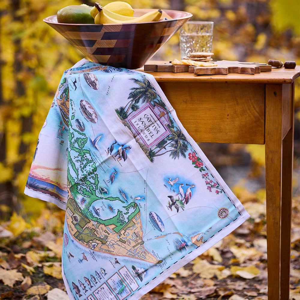 Map-themed towel draped over a wooden table with a bowl of fruit and glass in an autumn setting.