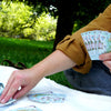 A person playing cards outside on a blanket in the grass. The cards have Sanibel and Captiva Florida Islands.