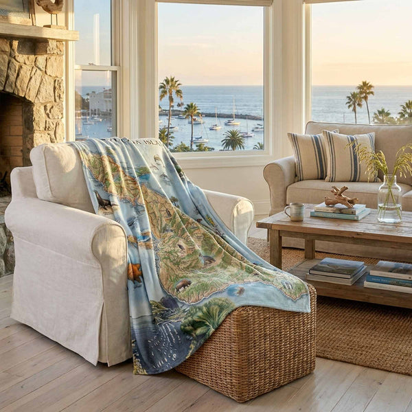Living room with a scenic blanket draped over a chair, large windows overlooking a harbor with palm trees.