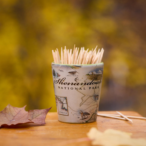 Shot glass with toothpicks and Shenandoah National Park design on a wooden surface with blurred natural background