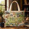 A canvas tote bag featuring a vintage-style illustrated map of Tennessee with the word 'TENNESSEE' across the top, displayed on a wooden table in a cozy indoor setting with books, a hat, sunglasses, and a mug nearby.