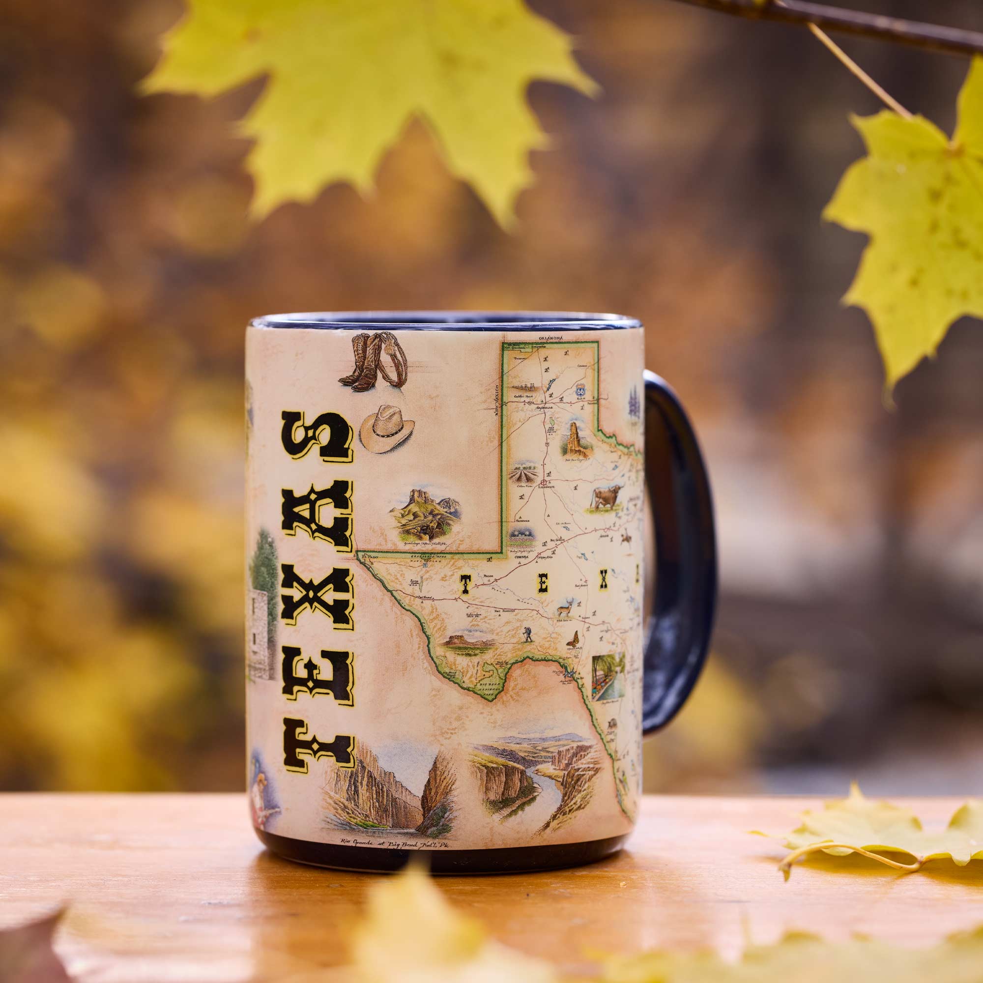 Mug with Texas-themed design on a wooden surface with autumn leaves.
