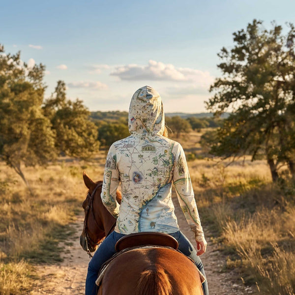 Person riding a horse on a dirt path through a scenic landscape with trees and open sky.