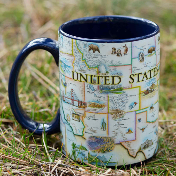USA Map Ceramic mug with handle sitting on grass in a forest. Blue - 16 oz.
