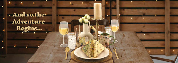 A table setting  for a weeding. The tablescape features a Montana Kitchen towel folded into a napkin. The table also features a Montana coffee mug, wine glasses, candle, flowers, and a deer antler for the table setting.  