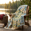 Map-themed blanket draped over a wooden chair by a lake with trees in the background