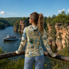 Person wearing a map-patterned jacket overlooking a scenic lake with a boat and cliffs.