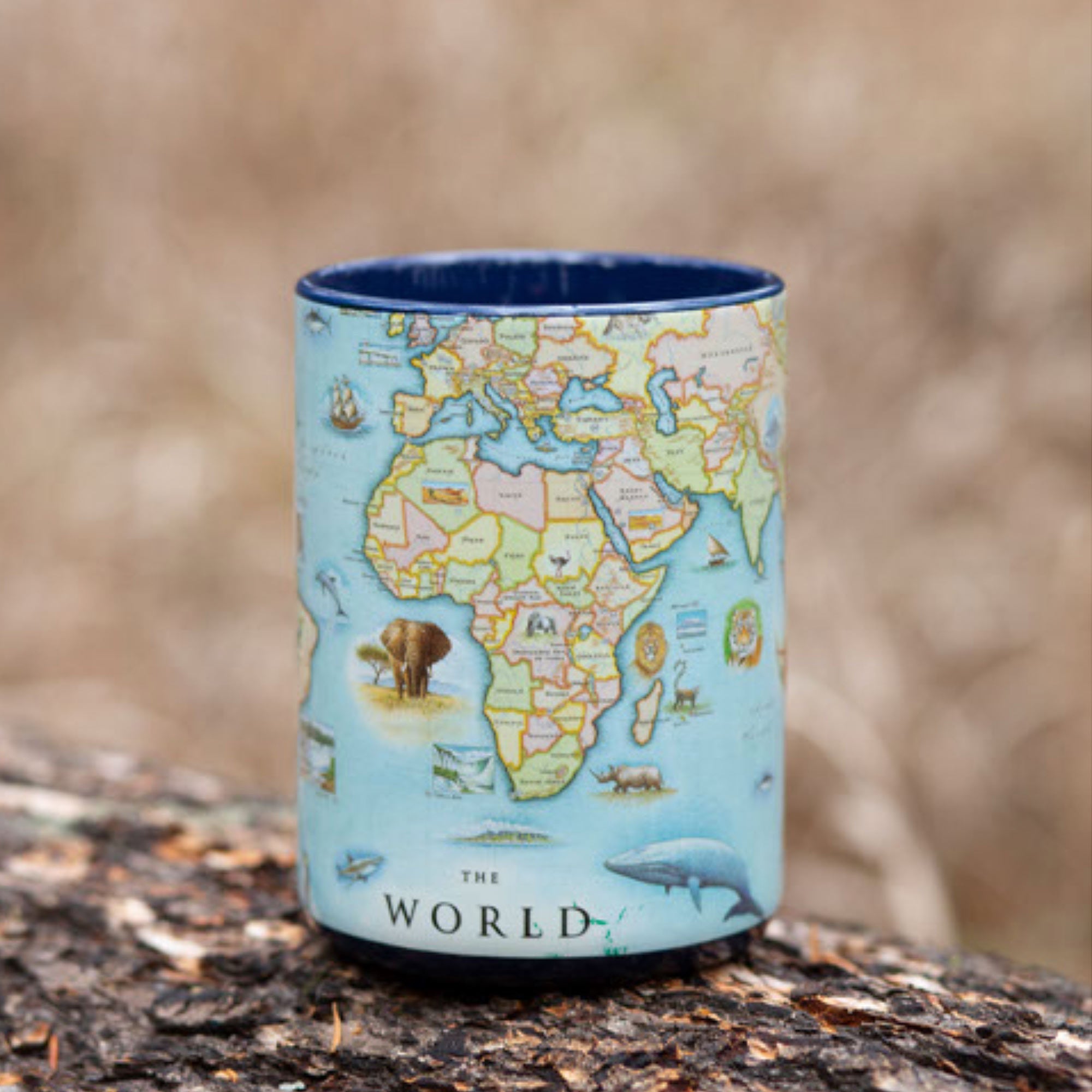 World Map Ceramic mug with handle sitting on a log in a forest. Blue - 16 oz.