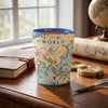 A ceramic mug printed with a vintage world map design sits on a wooden desk in a styled room setting with a window, notebook, globe, and compass.
