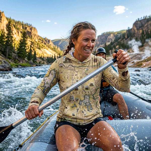Two people kayaking in a mountainous river landscape with Yellowstone national Park sun shirt on