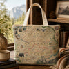 A canvas tote bag printed with an antique-style Yosemite National Park map, displayed on a wooden table in a cozy, rustic room setting with a window showing a mountain view.
