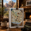 A 1000-piece jigsaw puzzle box for 'Zion National Park' is displayed on a wooden table in a cozy, rustic room with a fireplace, a mug, books, and binoculars. The background shows a scenic view of Zion's red rock canyons through a window.