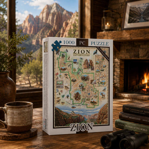 A 1000-piece jigsaw puzzle box for 'Zion National Park' is displayed on a wooden table in a cozy, rustic room with a fireplace, a mug, books, and binoculars. The background shows a scenic view of Zion's red rock canyons through a window.