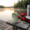 Green mug with map design on a wooden dock by a lake with sunset