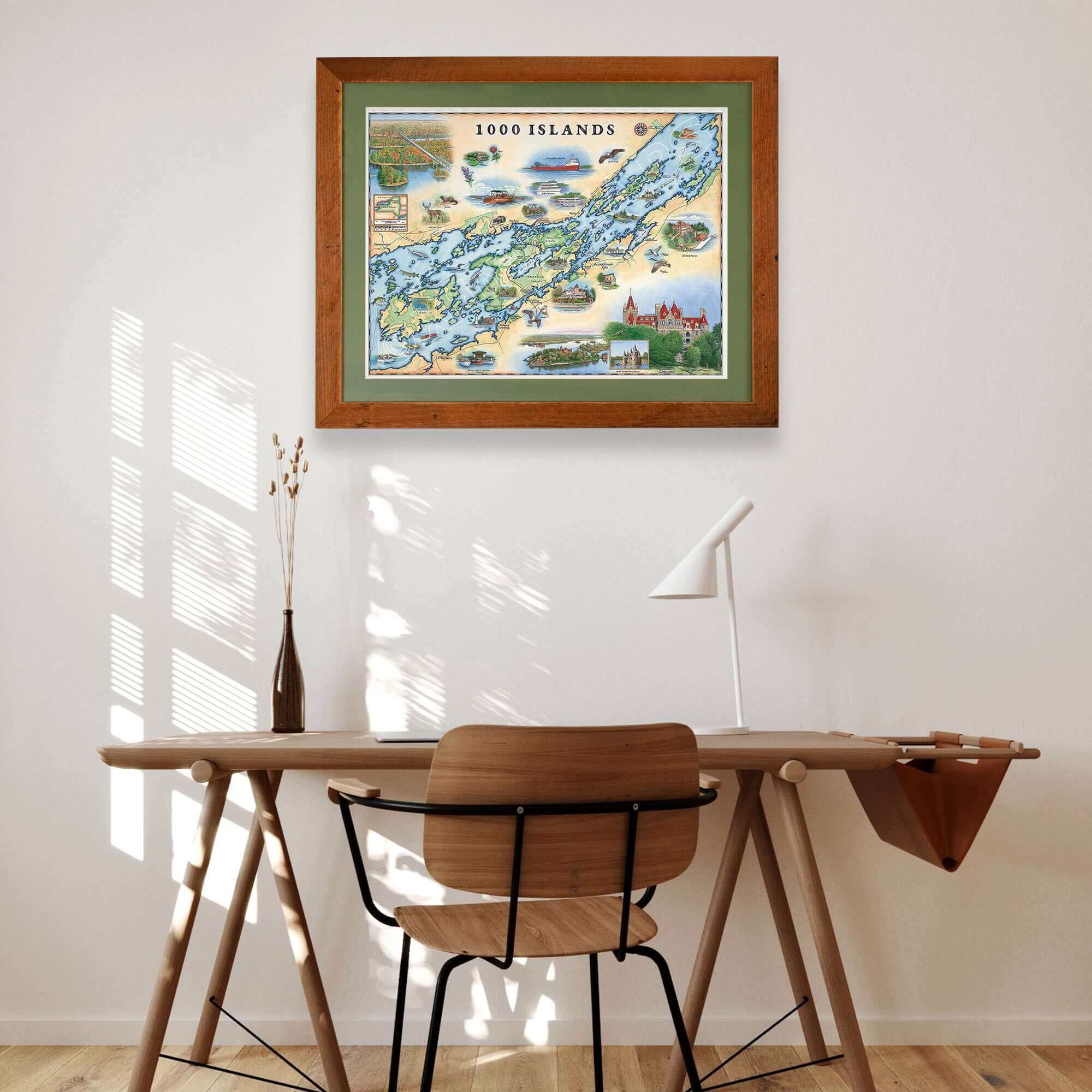 1000 Islands framed hand-drawn map with green mat hanging over a wooden desk and chair. 