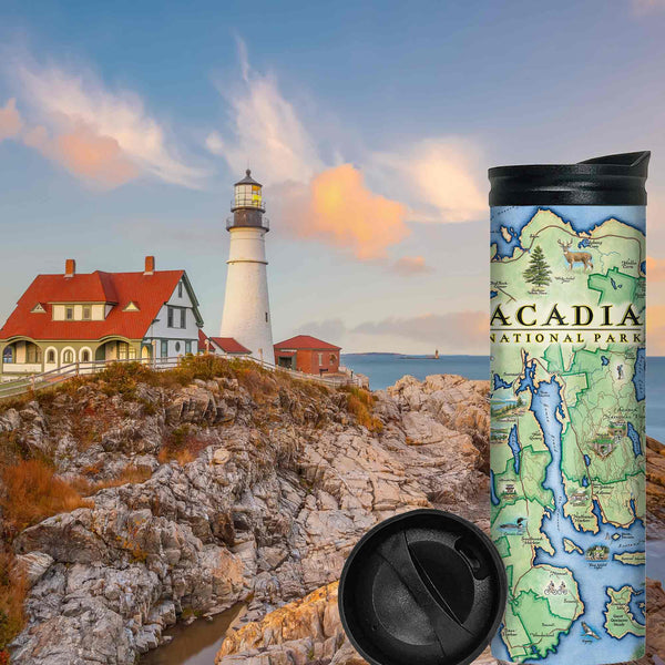 Maine's Acadia National Park Map -16 oz Travel Drinkware sitting on rocks by water during sunset. A lighthouse is sitting on the cliffs of Maine near the Atlantic ocean. 