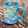 Maine's Acadia National Park Map Ceramic Mug in the color blue sitting on a log.  The coffee cup features Cadillac Mountains, Otter Cliffs, Beaver, and Jordon Pond. 