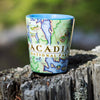 Maine's Acadia National Park Map Ceramic Shot Glass sitting on a tree stump. Blue 1.5 oz