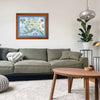 Alaska State map by xplorer maps hanging over a sage green couch. The print is framed in Montana Larch with blue mat. 