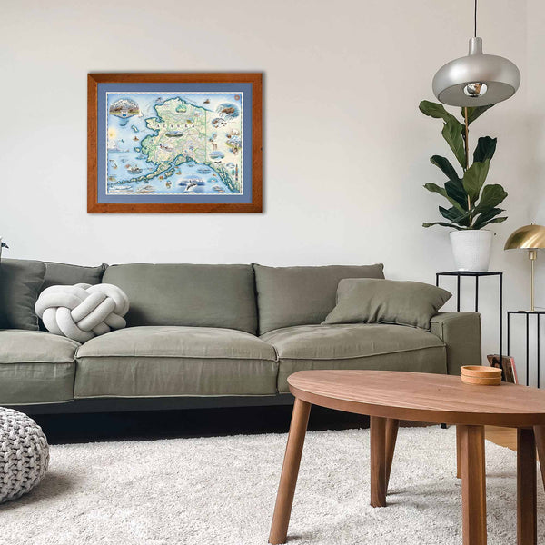 Alaska State map by xplorer maps hanging over a sage green couch. The print is framed in Montana Larch with blue mat. 