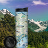 Alaska State Map 16 oz Travel Drinkware in earth tone colors sitting on rocks by water during sunset or sunrise.