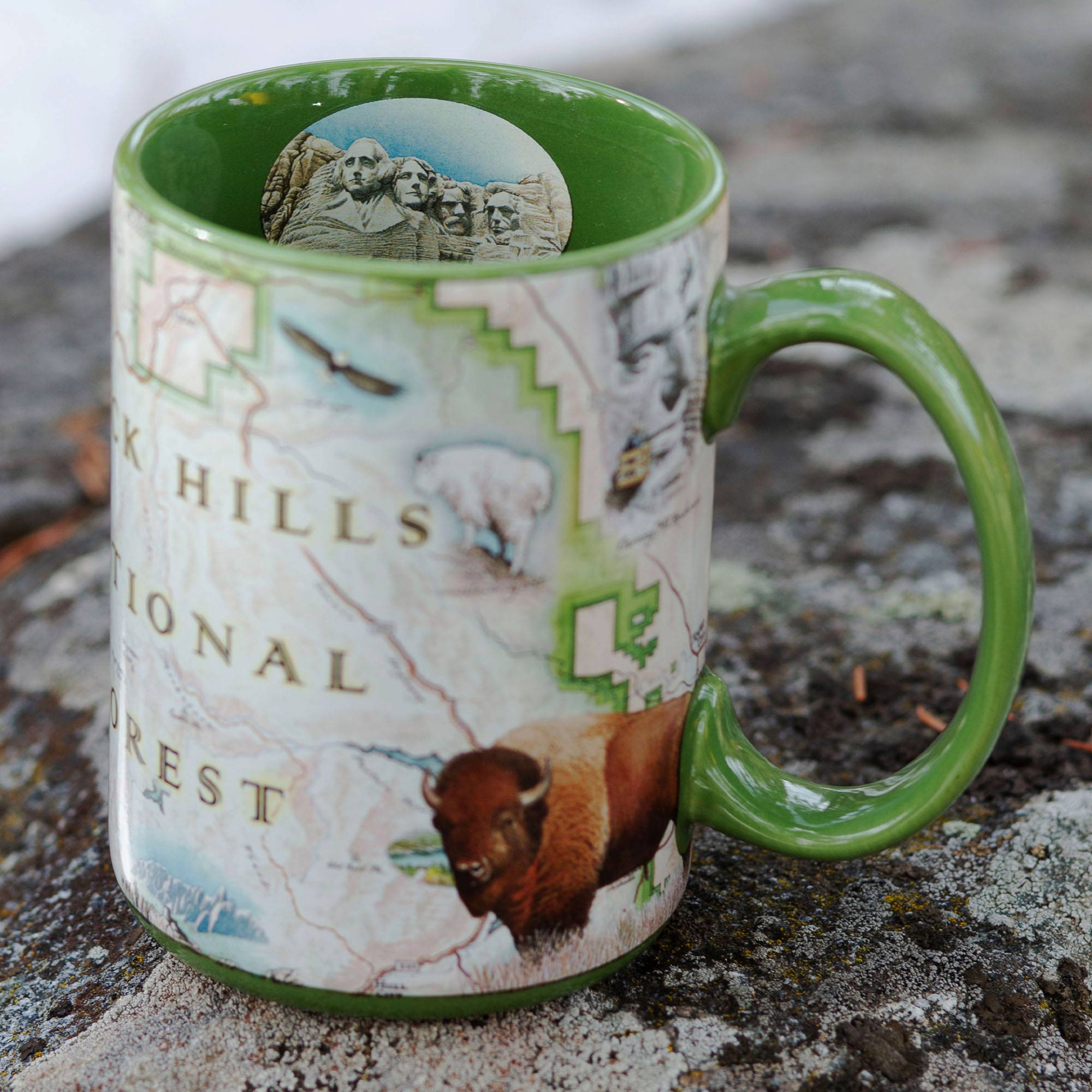  Black Hills National Forest Map ceramic mug sitting on a rock with Mount Rushmore seen on the cup - 16 oz, Green 