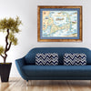 Massachusetts' Cape Cod Hand-Drawn Map hanging over a blue couch.  Featuring Plymouth Rock, fish, crane, fox, Provincetown, canoeing, biking, beach, and ocean.