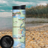 Travel Drinkware sitting on the pebble beach of Chesapeake Bay. With the Ocean and a tree in the background. The map is featuring illustrations of boat craft and marine life. Places on the map include Baltimore, Annapolis, Cambridge, Yorktown, and the Chesapeake Bay Bridge.
