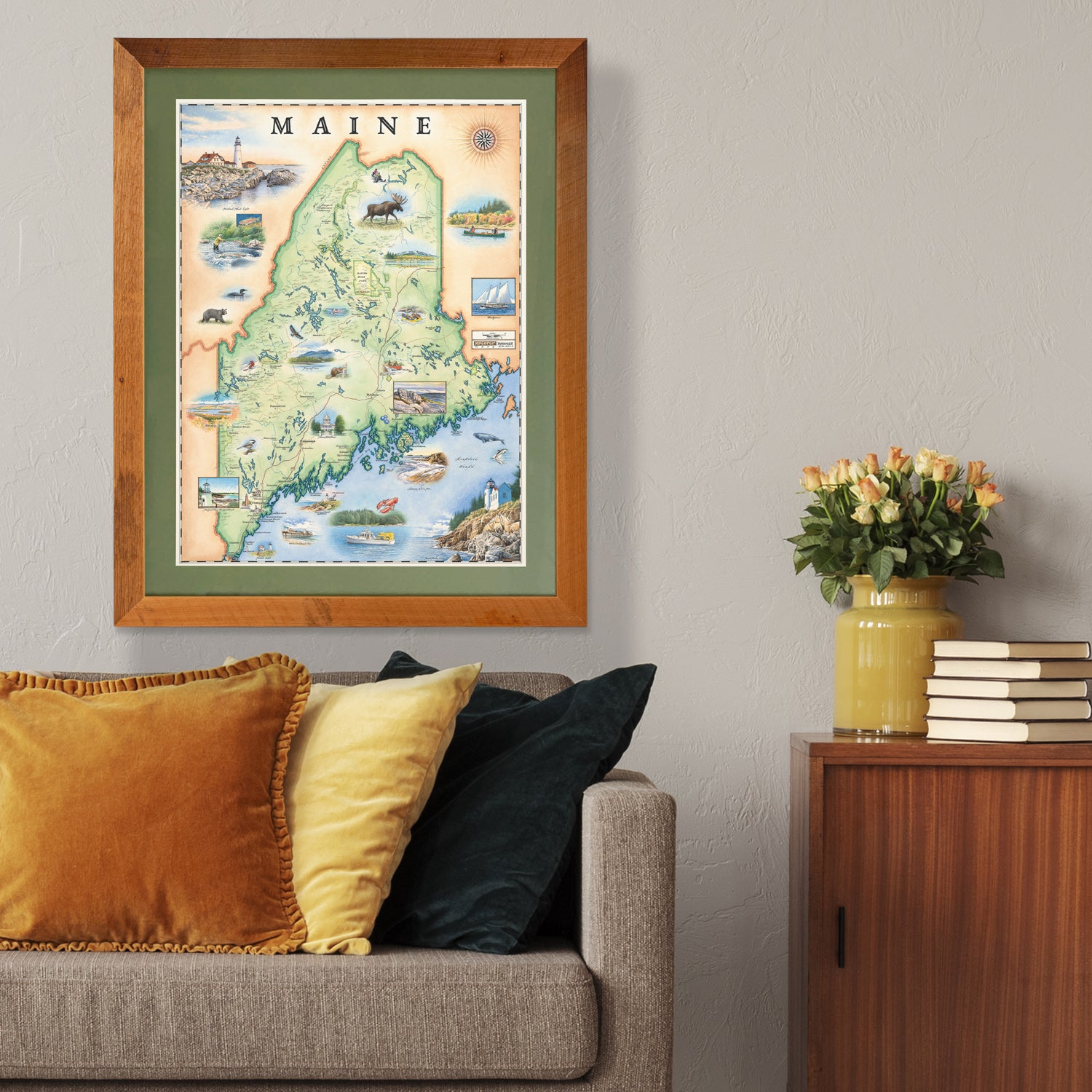 Xplorer Maps state map of Maine hangs in a living room above a gray couch with orange pillows. 