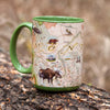 Green 16 oz Montana state map ceramic coffee mug sitting on a tree log. The cup features bison, Grizzly bears, moose, dinosaurs, Lewis and Clark, Fort Peck, cowboys, First Nation people, Crow lands, Helena, Bozeman, Missoula, Billings, Whitefish, Pronghorn, bald eagle, and trout.