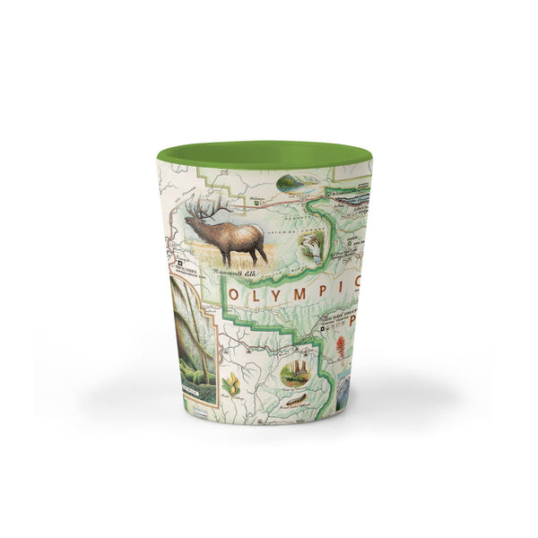 Olympic National Park Map Ceramic shot glass by Xplorer Maps. The map features illustrations of the park such as Enchanted Valley Chalet, Sol Duc Hot Springs Resort, Hurricane Ridge Visitor Center, and Kalaloch Lodge. Flora and fauna include sea otters, Roosevelt elk, Chinook salmon, skunk cabbage, and Flett's Violet.