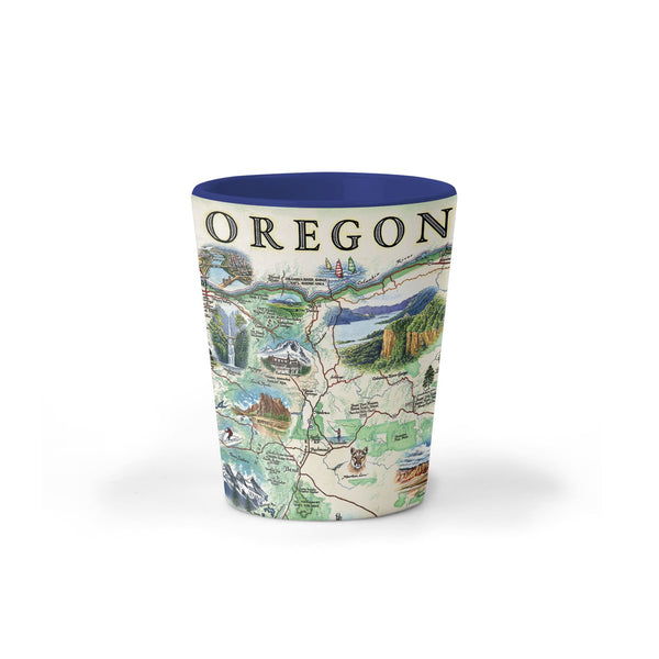 Oregon Map Ceramic shot glass by Xplorer Maps. The map features illustrations such as Hells Canyon Snake River, the Columbia River Gorge, Multnomah Falls, and Crater Lake. Flora and fauna include blue whales, big horn sheep, Dungeness crab, Oregon grape, and Douglas Fir. Some cities depicted are Portland, Hood River, Cannon Beach, and Seaside. 