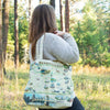 Women in the woods carrying a Pennsylvania Canvas Tote bag by Xplorer Maps. The tote features Philadelphia, Pittsburgh, Hershey Park, and Pocono Mountains. Flora and fauna include deer, Punxsutawney Phil, and squirrels.