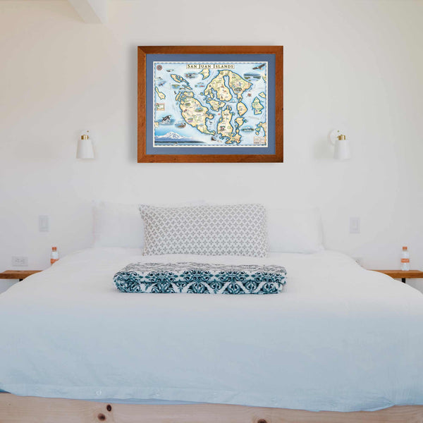 The San Juan Islands hand-drawn map hanging on a white wall over a bed with a white comforter and a blue throw blanket. 