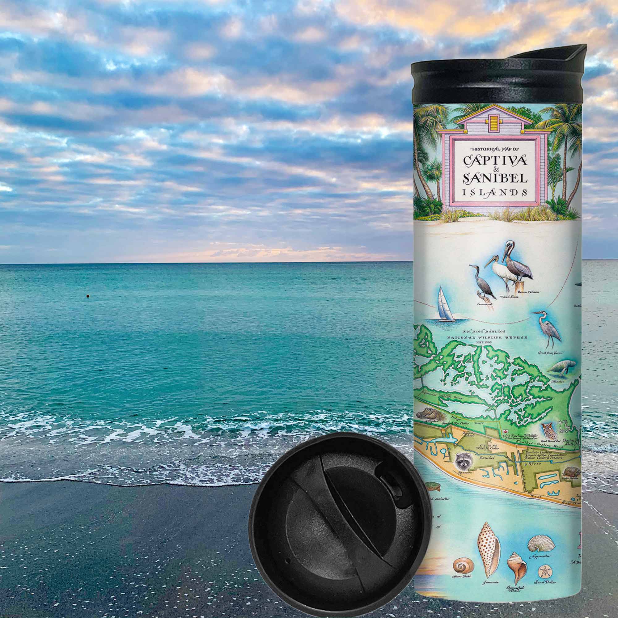 Florida's Sanibel & Captiva Islands Map Travel Drinkware sitting on a beach with ocean and clouds in the background. The map features illustrations of places such as Ding Darling Wildlife Sanctuary, Bailey-Matthews Shell Museum, and Sanibel Lighthouse. Flora and fauna include the Loggerhead sea turtle, Manatee, and Great Blue Heron. Many other birds and sea animals are illustrated.