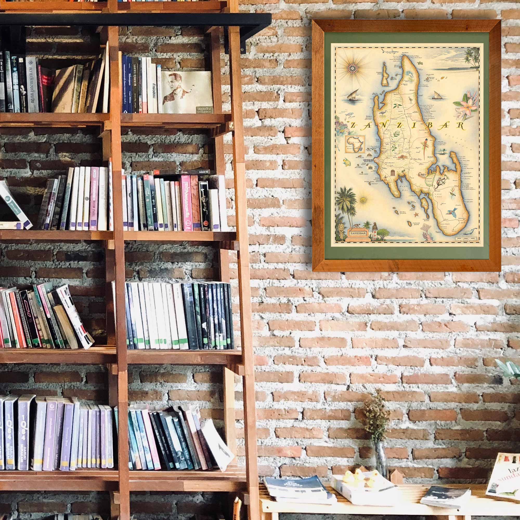 Africa's Zanzibar framed hand-drawn map is hanging on a brick wall next to a large shelf unit with a ladder. 